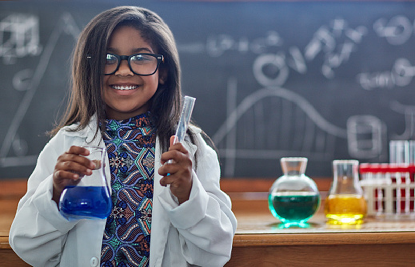 A student in a lab coat holding flasks of colored liquid