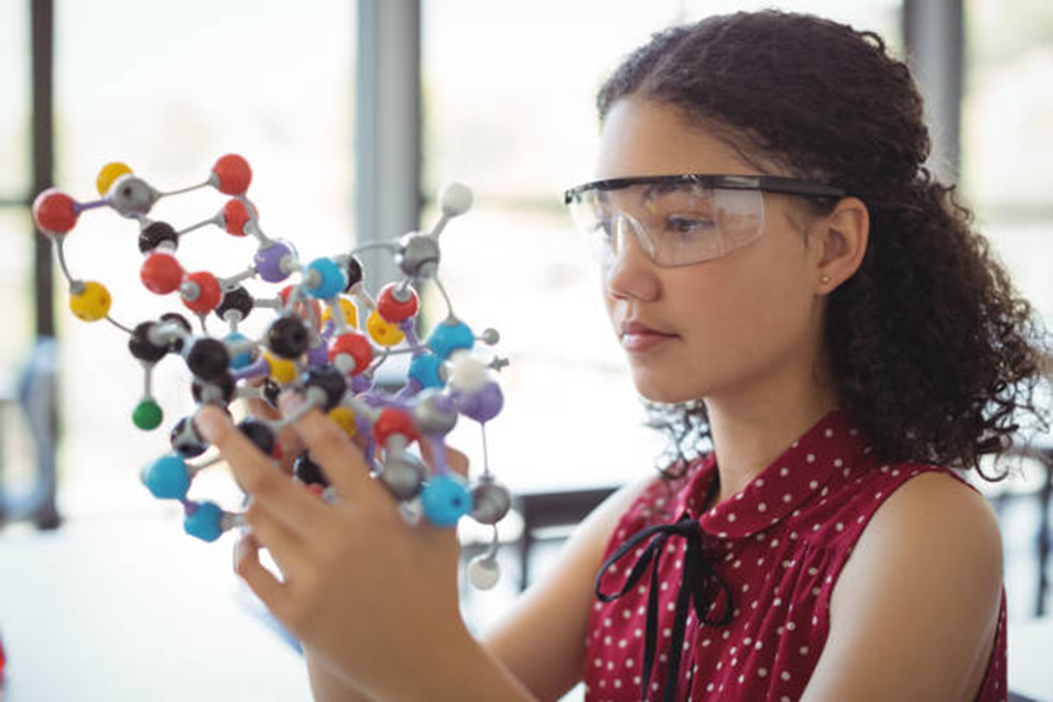 A student in safety glasses studying a large molecule model
