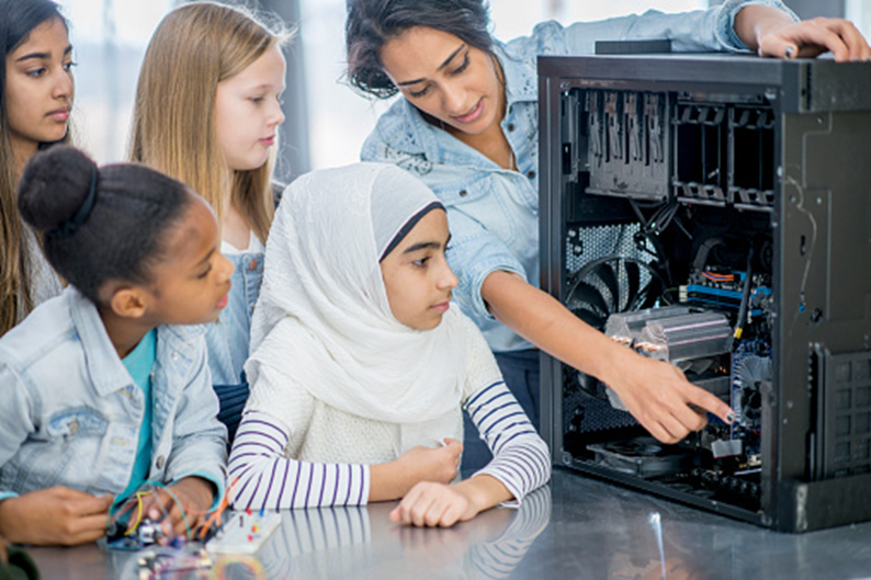 Students watching a teacher point out parts inside a computer